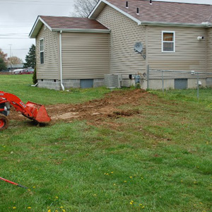 Excavator replaces soil on top of dry well next to a residential home